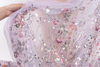 A hand is holding up a delicate, intricately embroidered fabric with a floral pattern.