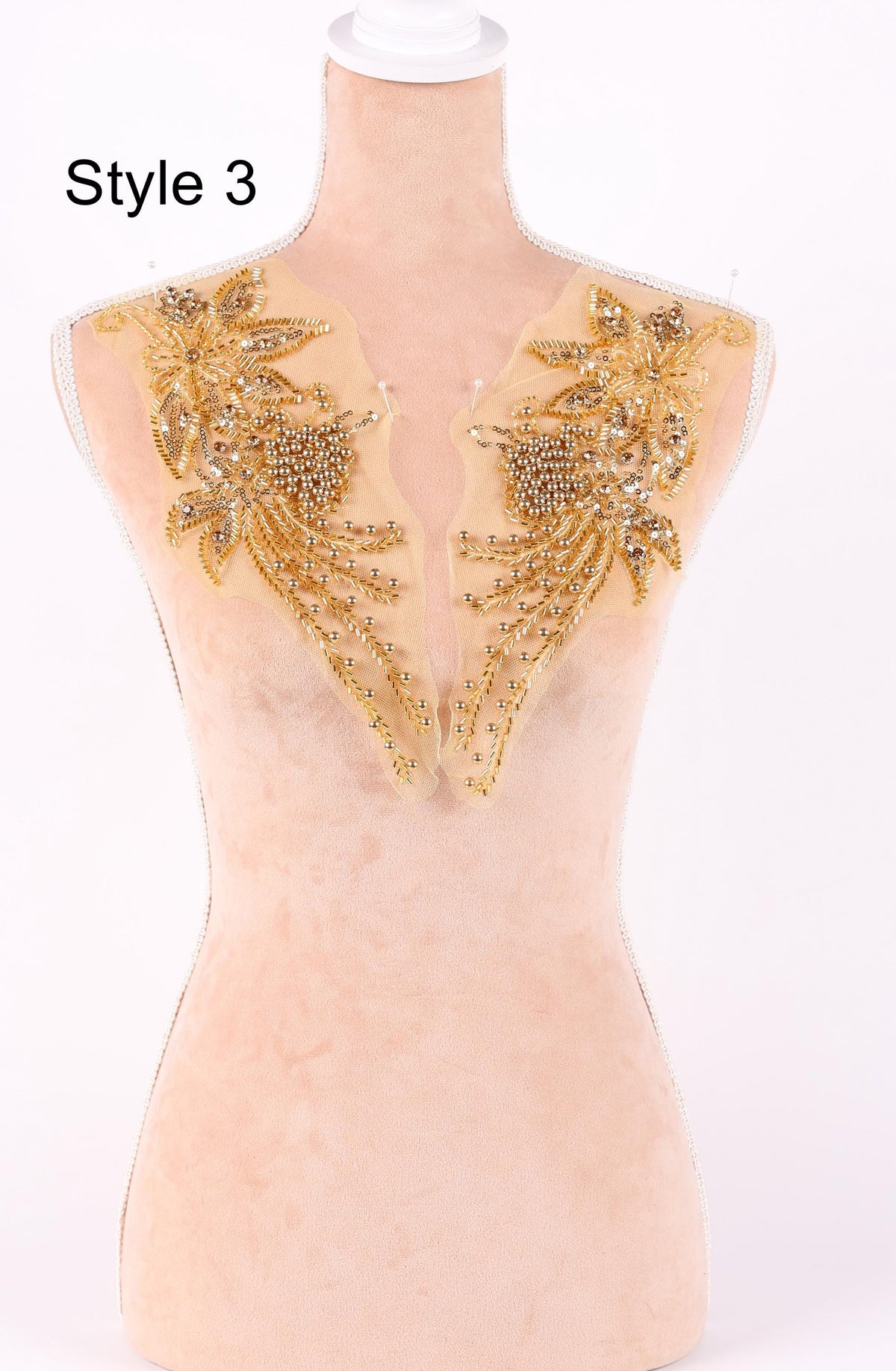 A mannequin with a beige body and gold embellishments on its shoulders, including flowers and leaves.