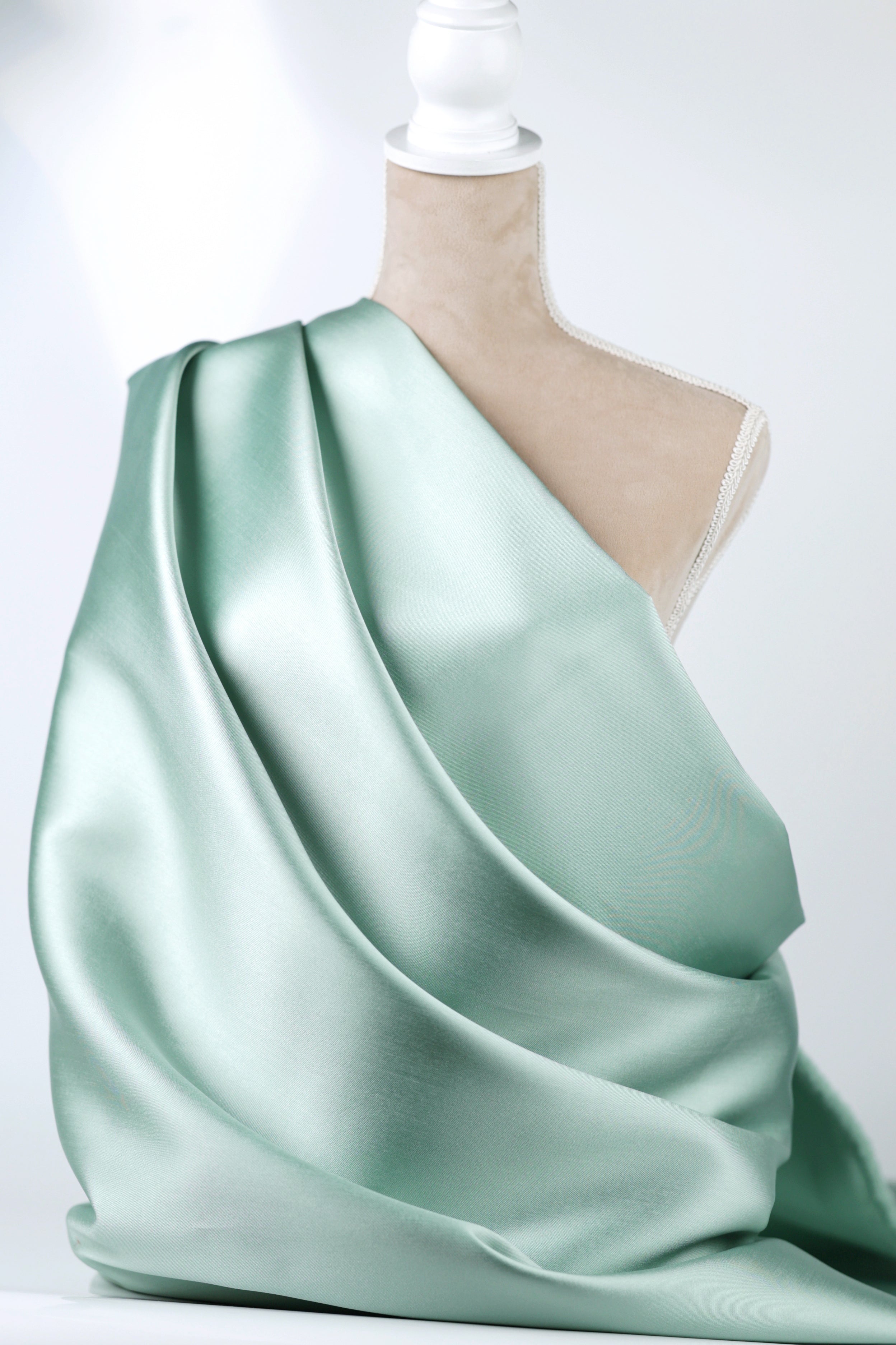 A mannequin wearing a flowing, mint green satin fabric draped over its body.