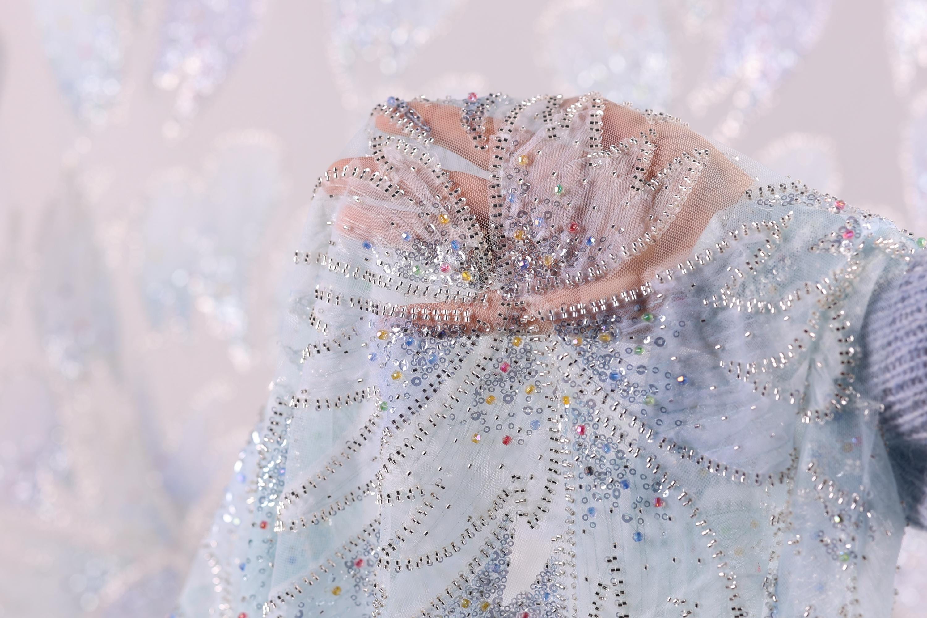 A close-up view of a hand holding a delicate, intricately beaded fabric.