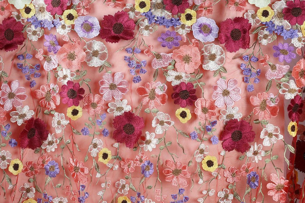 a close-up view of a fabric with a vibrant floral pattern. The fabric is adorned with a variety of colorful flowers, including red, pink, purple, yellow, and white flowers, all intricately embroidered or stitched onto the fabric. The flowers are arranged in a visually appealing manner, creating a lively and eye-catching design.