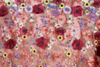 a close-up view of a fabric with a vibrant floral pattern. The fabric is adorned with a variety of colorful flowers, including red, pink, purple, yellow, and white flowers, all intricately embroidered or stitched onto the fabric. The flowers are arranged in a visually appealing manner, creating a lively and eye-catching design.