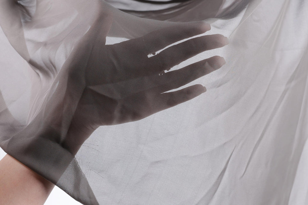A hand is holding a piece of sheer, light gray fabric, which appears to be a type of chiffon or sheer material.