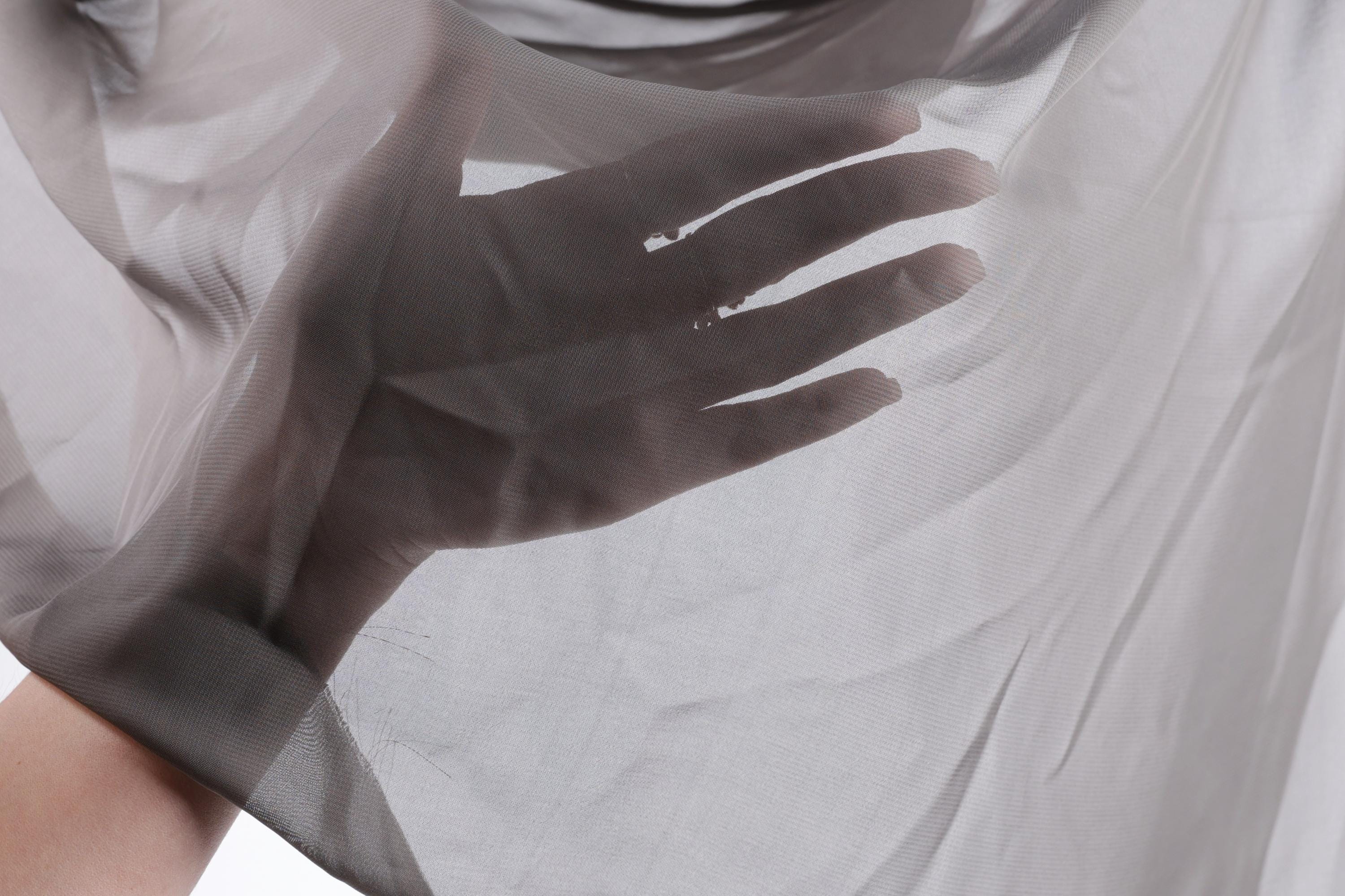 A hand is holding a piece of sheer, light gray fabric, which appears to be a type of chiffon or sheer material.