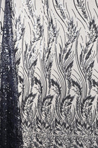 a close-up view of a fabric with a repeating pattern of black and white floral designs. The pattern consists of various leaf-like shapes and lines, creating a visually striking and intricate design. The fabric appears to be made of a material with a shimmering or sequined effect, adding a touch of elegance and sophistication to the overall appearance.