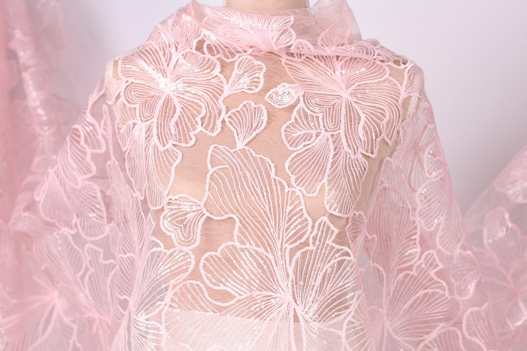 A close-up view of a delicate, pink lace fabric with a floral pattern.