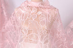 A close-up view of a delicate, pink lace fabric with a floral pattern.