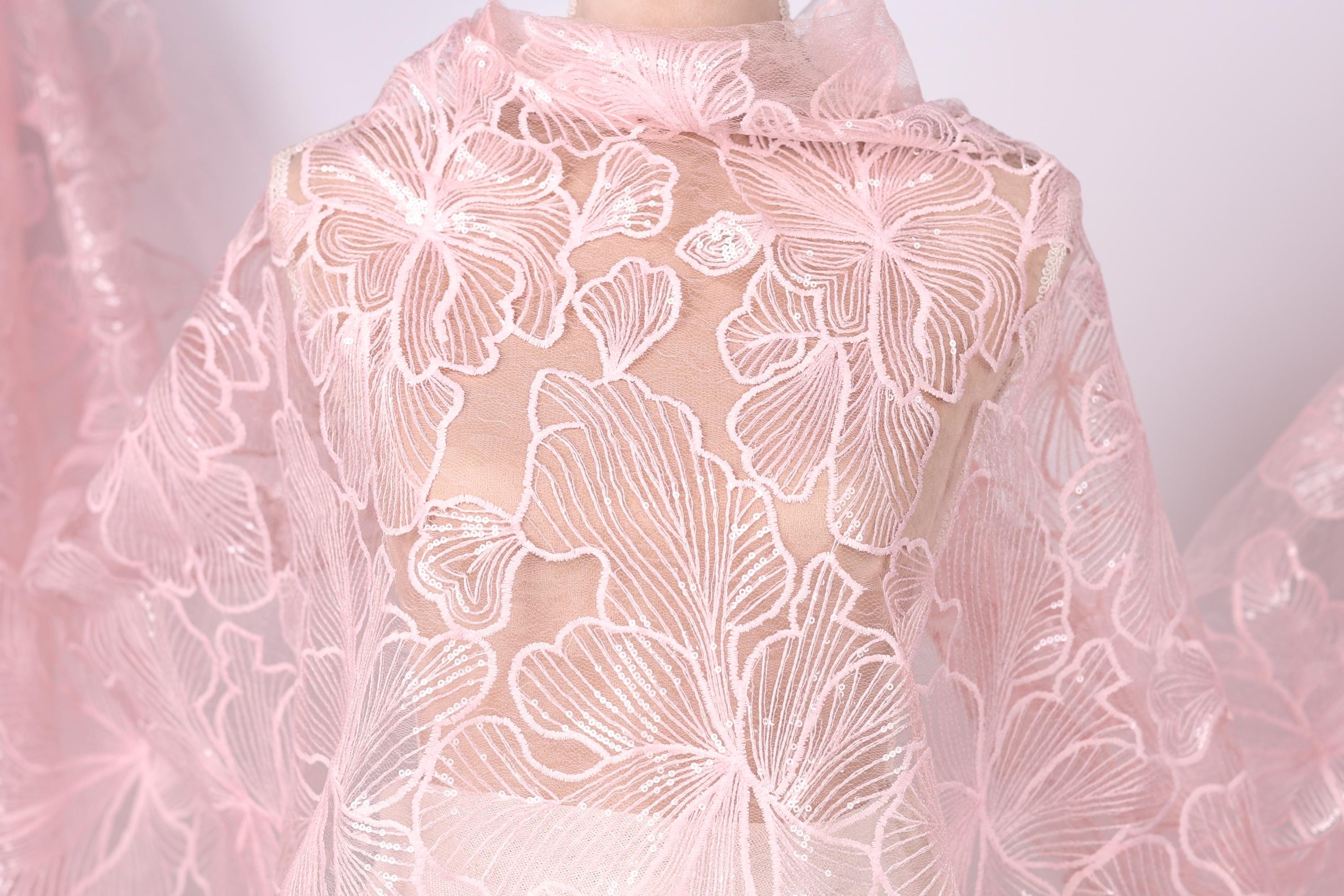 A close-up view of a delicate, pink lace fabric with a floral pattern.