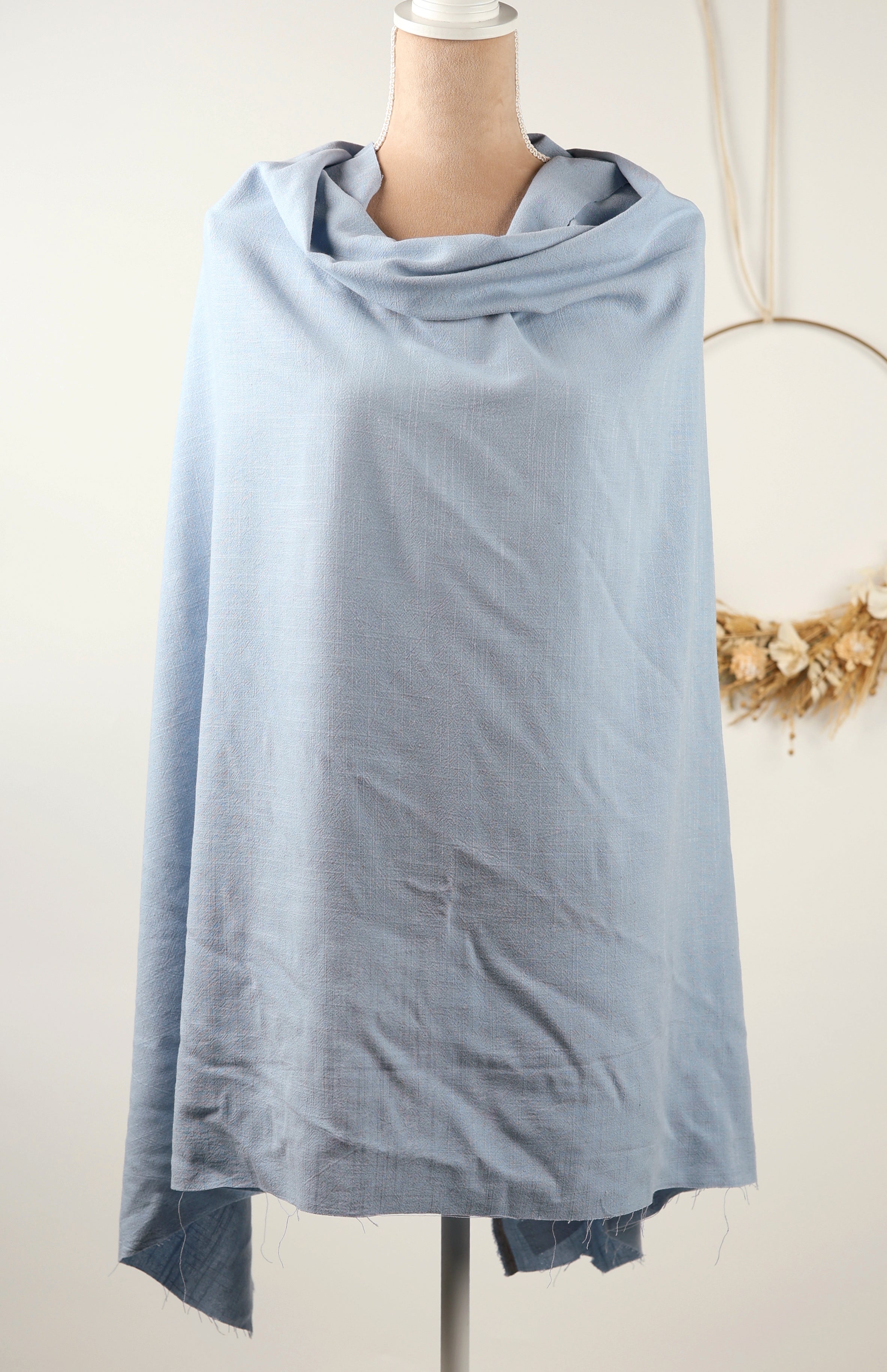 A light blue draped garment is displayed on a mannequin against a white background.