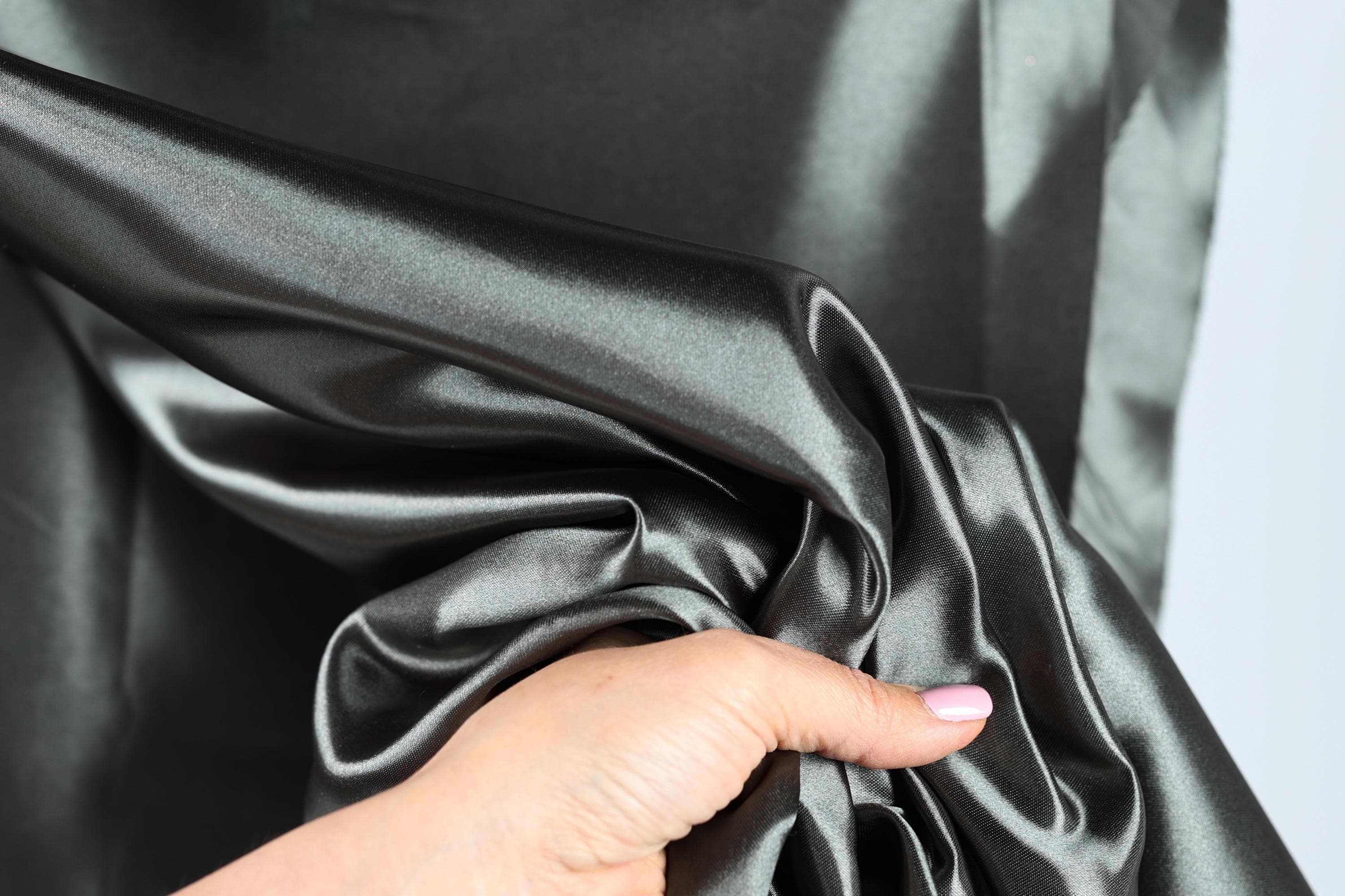 A hand is holding a piece of shiny, dark grey satin fabric, with the fabric partially draped over the hand.