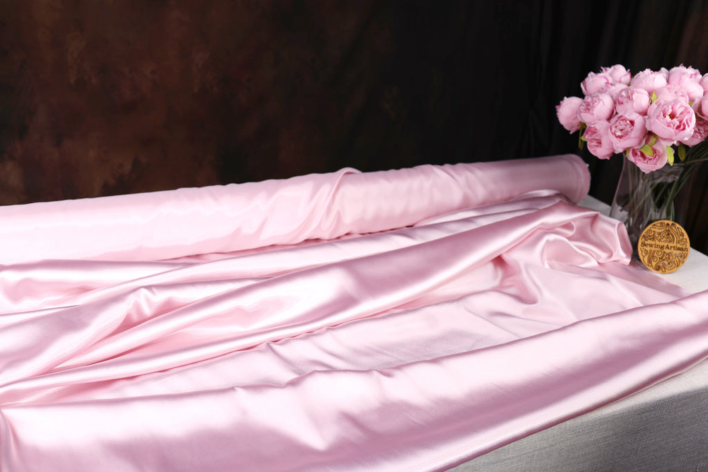a pink satin fabric draped over a table, with a vase of pink flowers placed next to it.