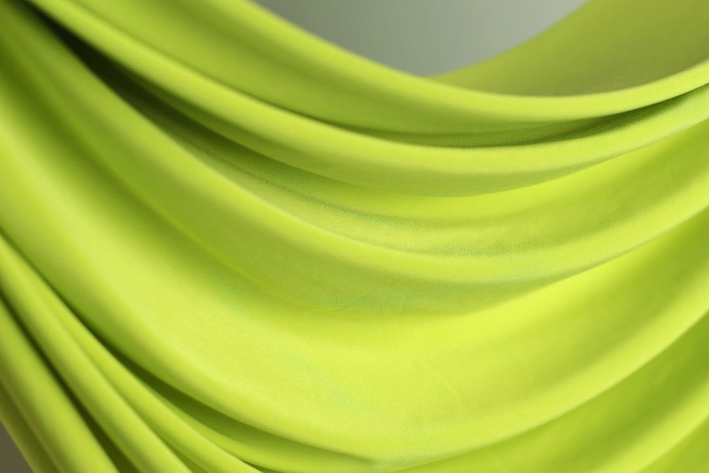 A close-up view of a bright green fabric, possibly a sheer or sheer-like material, with a smooth, flowing texture.