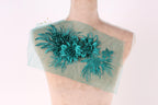 A mannequin with a green floral embroidered on its shoulder, set against a plain white background.