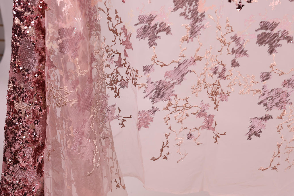 a close-up view of a delicate, pink and white fabric with a floral pattern. The fabric appears to be made of sheer material, giving it a soft and delicate appearance. The floral pattern is intricate and detailed, adding a touch of elegance to the fabric. The image does not contain any text or other objects, and the focus is solely on the fabric and its design.