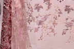 a close-up view of a delicate, pink and white fabric with a floral pattern. The fabric appears to be made of sheer material, giving it a soft and delicate appearance. The floral pattern is intricate and detailed, adding a touch of elegance to the fabric. The image does not contain any text or other objects, and the focus is solely on the fabric and its design.