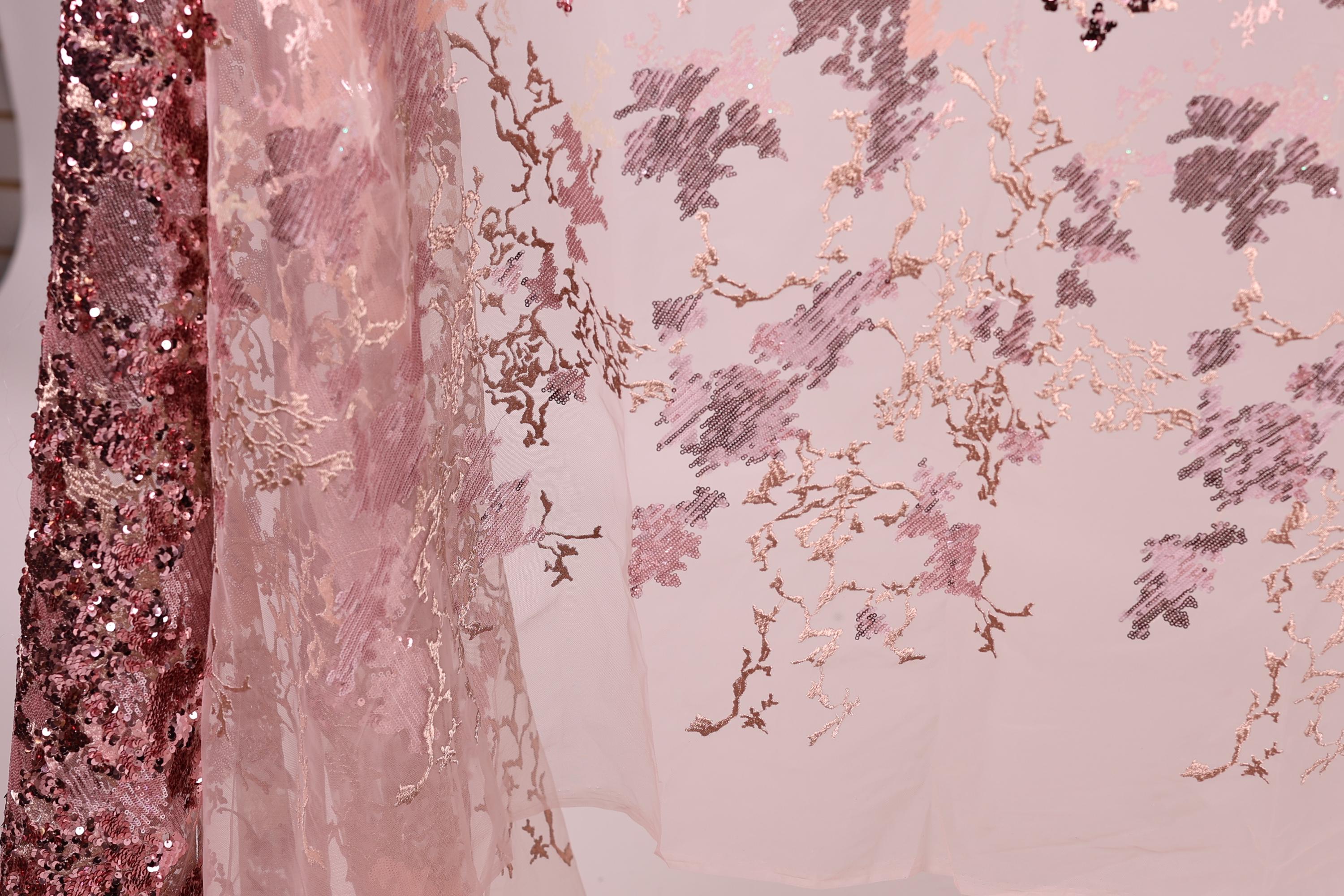 a close-up view of a delicate, pink and white fabric with a floral pattern. The fabric appears to be made of sheer material, giving it a soft and delicate appearance. The floral pattern is intricate and detailed, adding a touch of elegance to the fabric. The image does not contain any text or other objects, and the focus is solely on the fabric and its design.