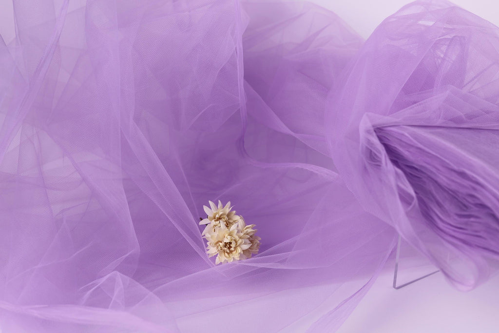 a small white flower resting on a purple fabric, which appears to be a sheer or sheer-like material.
