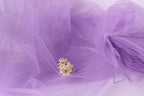 a small white flower resting on a purple fabric, which appears to be a sheer or sheer-like material.