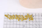 a close-up view of a gold embroidered leaf design placed on a ruler, indicating that it is being measured or sized for a sewing or crafting project.