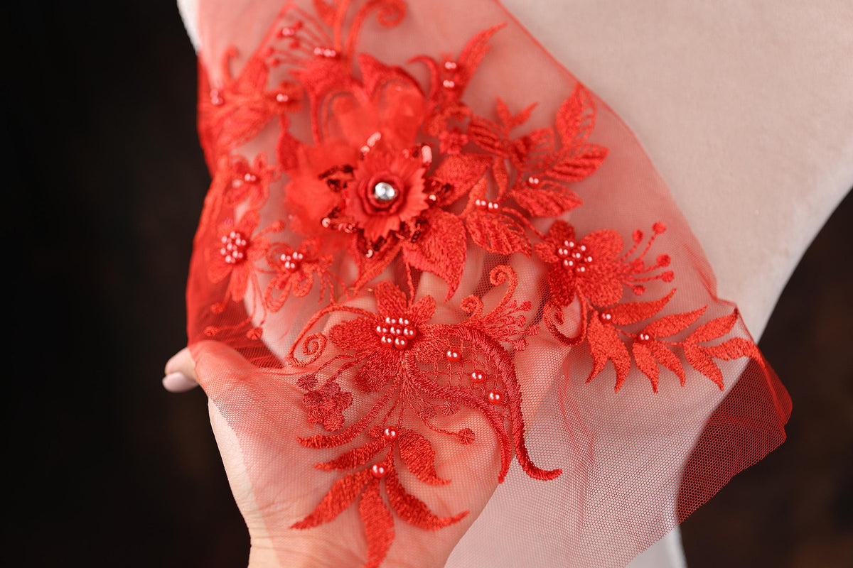 A hand holding a piece of red lace with intricate floral embroidery.