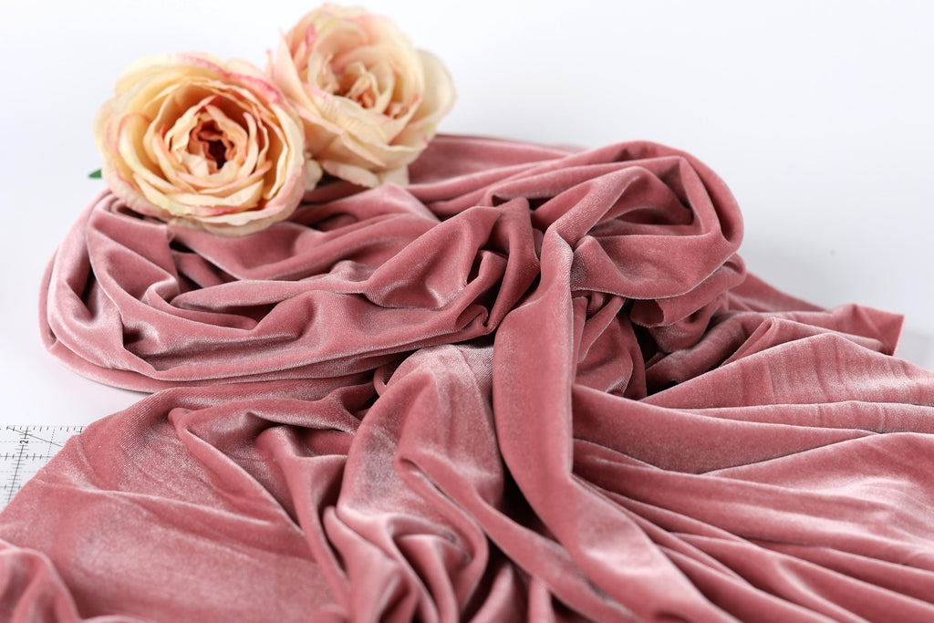 a close-up view of a pink velvet fabric with two light pink roses resting on top of it.