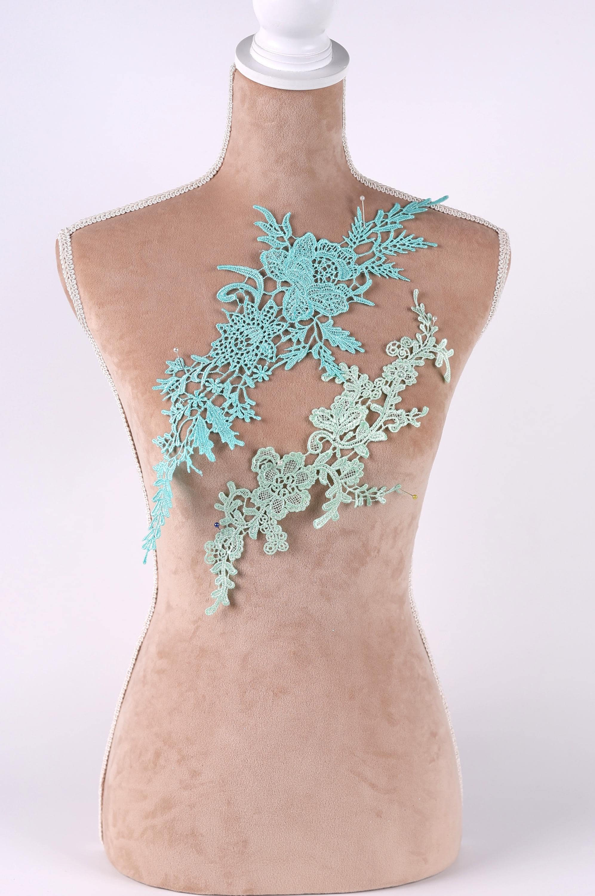 A mannequin torso with a decorative green lace piece sewn onto it.