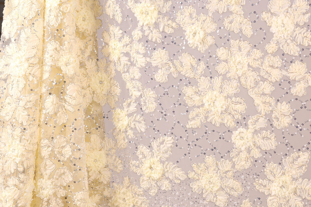 a close-up view of a fabric with a floral pattern, including white and yellow flowers and sequins. The fabric appears to be made of a sheer material, giving it a delicate and elegant appearance.