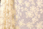 a close-up view of a fabric with a floral pattern, including white and yellow flowers and sequins. The fabric appears to be made of a sheer material, giving it a delicate and elegant appearance.