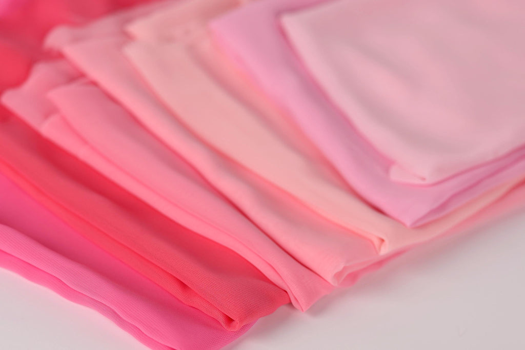 A close-up image of various shades of pink fabric, including a light pink, a darker pink, and a pale pink, arranged in a visually appealing manner.