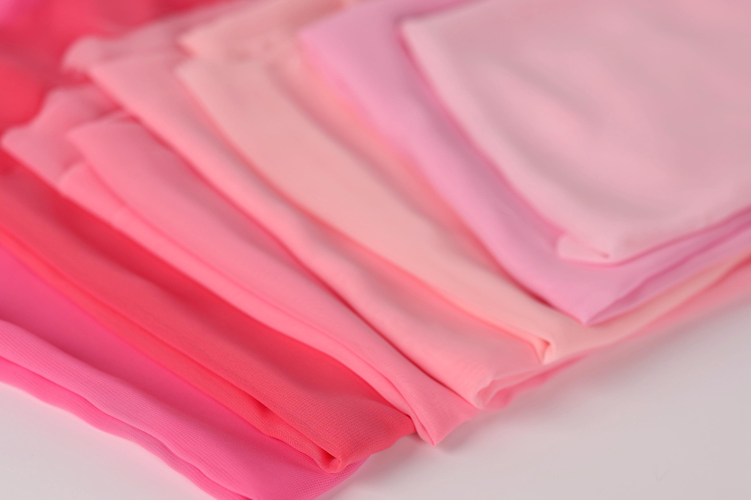 A close-up image of various shades of pink fabric, including a light pink, a darker pink, and a pale pink, arranged in a visually appealing manner.