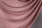 a close-up view of a soft, flowing pink fabric, possibly a satin or velvet material. The fabric appears to be draped or swirled, creating a sense of movement and elegance.