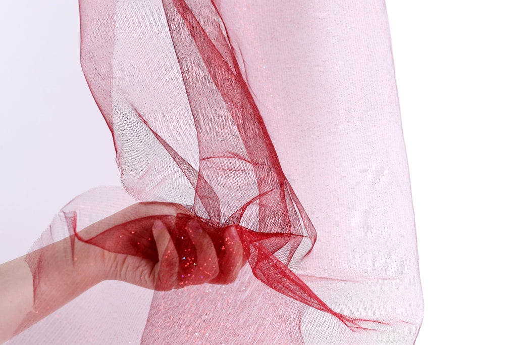 A hand is holding a red, shiny fabric with a delicate, flowing texture.