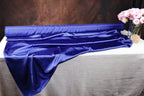 a roll of blue satin fabric placed on a table, with a vase of pink flowers next to it.