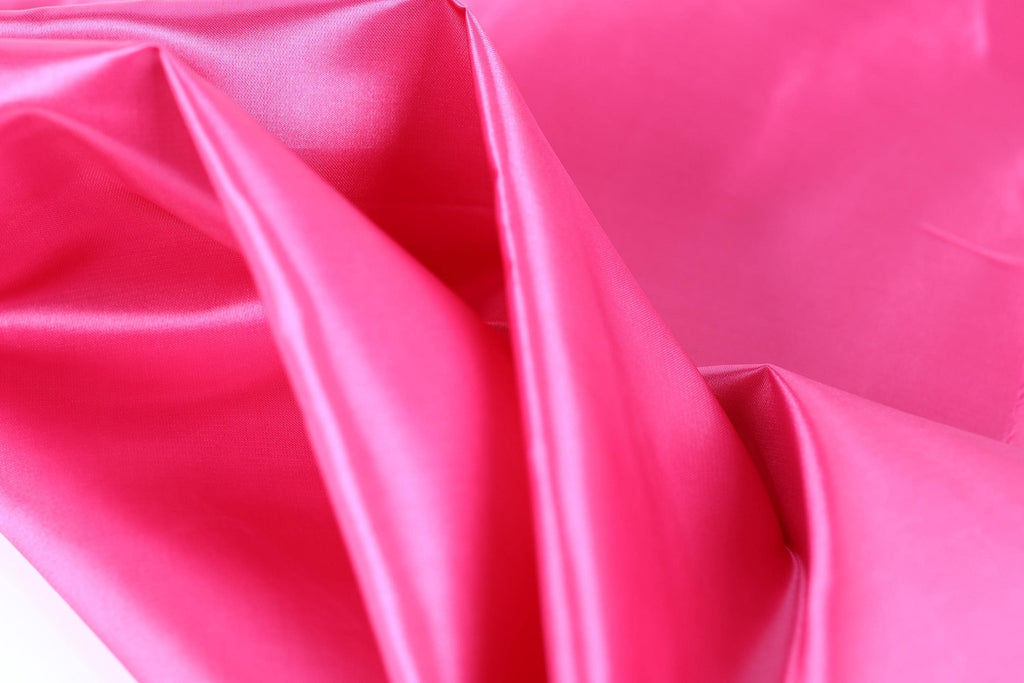 The image is a close-up of a bright pink fabric, with a smooth and shiny texture.