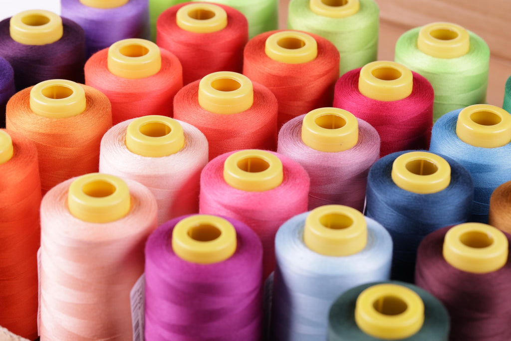 A close-up image of a collection of colorful spools of thread with yellow caps, arranged in rows.