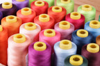 A close-up image of a collection of colorful spools of thread with yellow caps, arranged in rows.