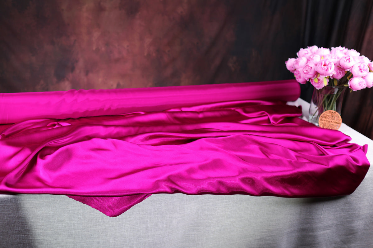 a large roll of pink satin fabric, a vase filled with pink flowers, and a dark background.