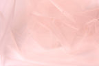 The image is a close-up of a soft, light pink fabric, possibly tulle, with a slightly wrinkled texture.
