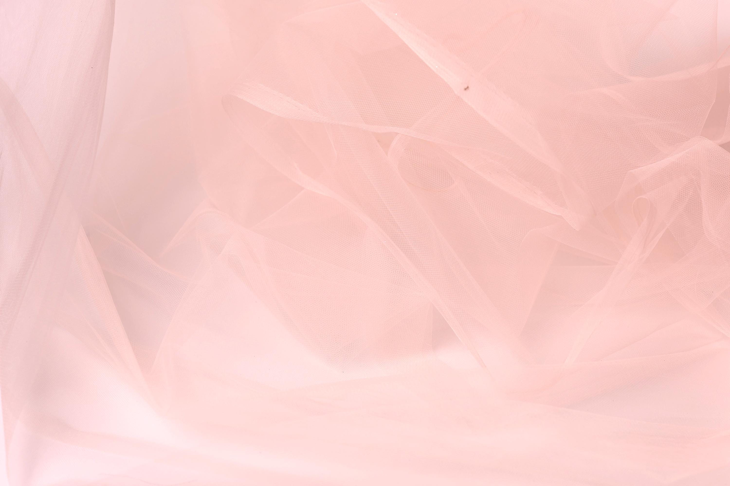 The image is a close-up of a soft, light pink fabric, possibly tulle, with a slightly wrinkled texture.
