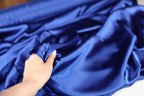 A hand is holding a piece of blue satin fabric, examining it closely.