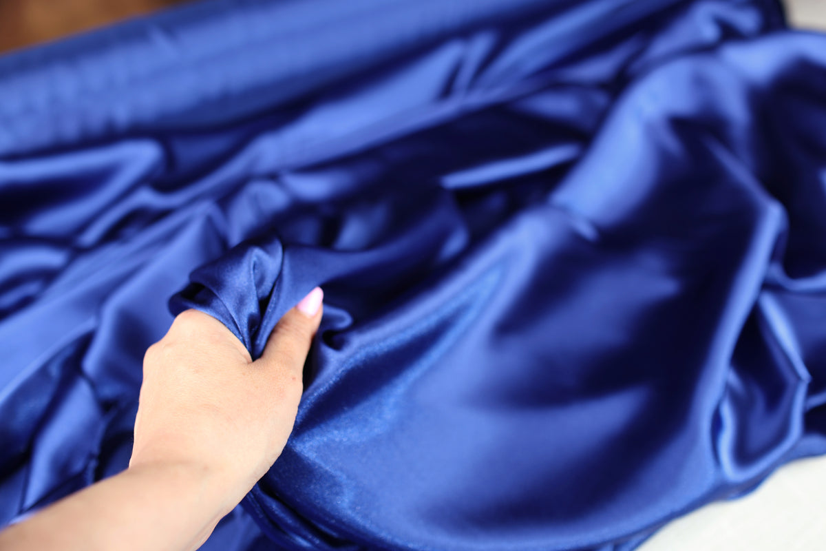 A hand is holding a piece of blue satin fabric, examining it closely.