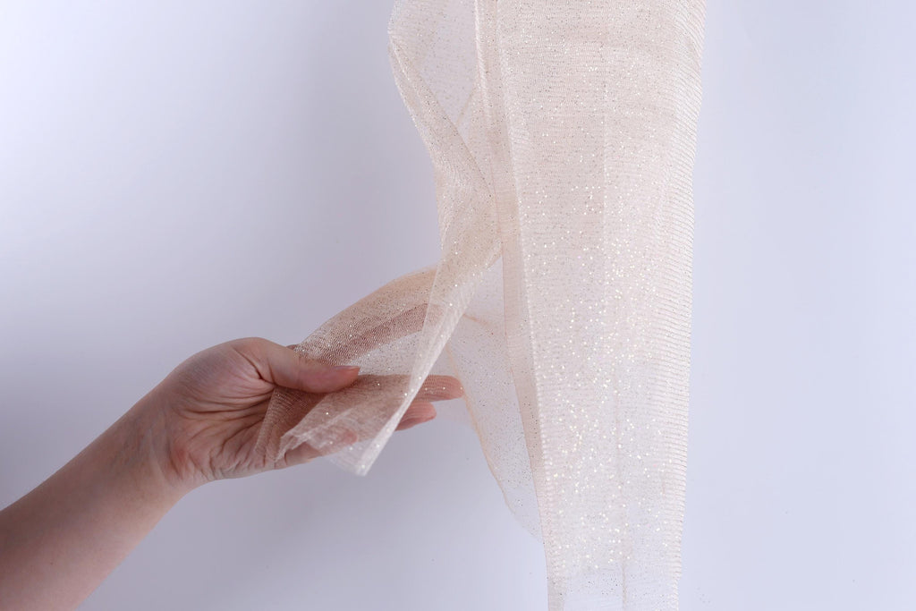 A hand is holding a piece of beige, shiny fabric or material with a textured appearance.