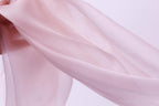 A close-up view of a soft, flowing pink fabric, possibly silk or chiffon, against a plain white background.