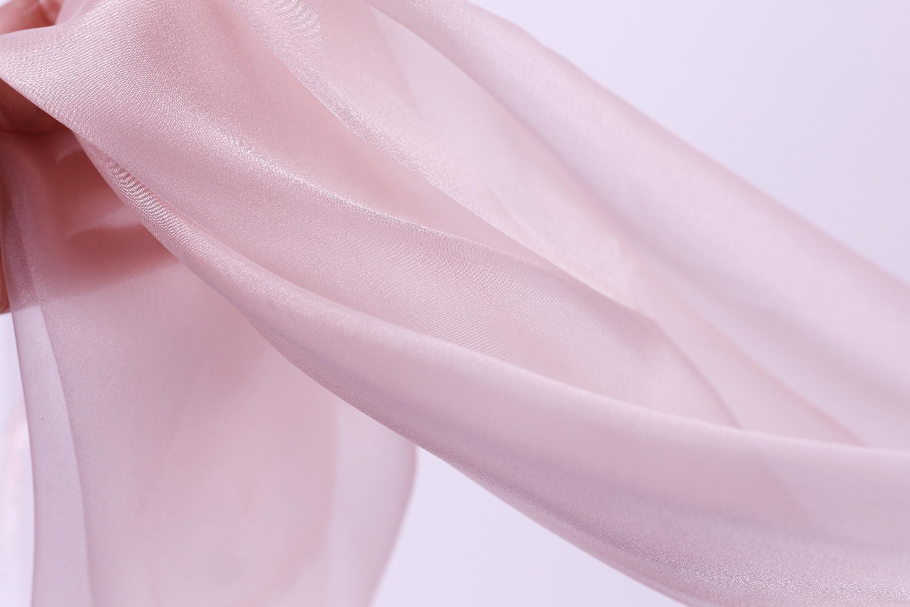 A close-up view of a soft, flowing pink fabric, possibly silk or chiffon, against a plain white background.