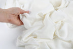 A hand is holding a white fabric, possibly cotton, and appears to be examining it closely.