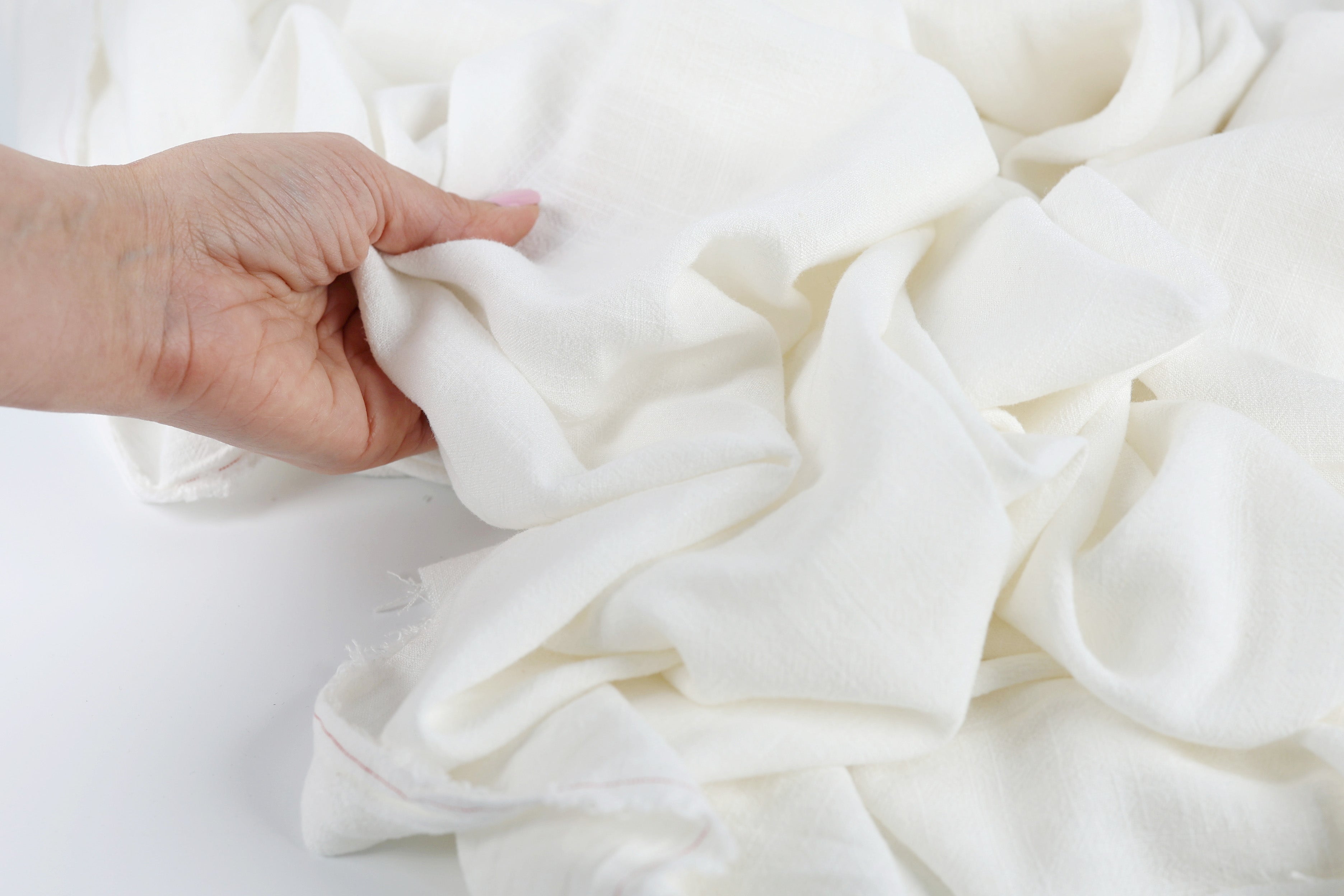A hand is holding a white fabric, possibly cotton, and appears to be examining it closely.