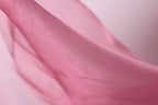 A close-up view of a soft, flowing pink fabric, possibly silk or chiffon, with a smooth and shiny texture.