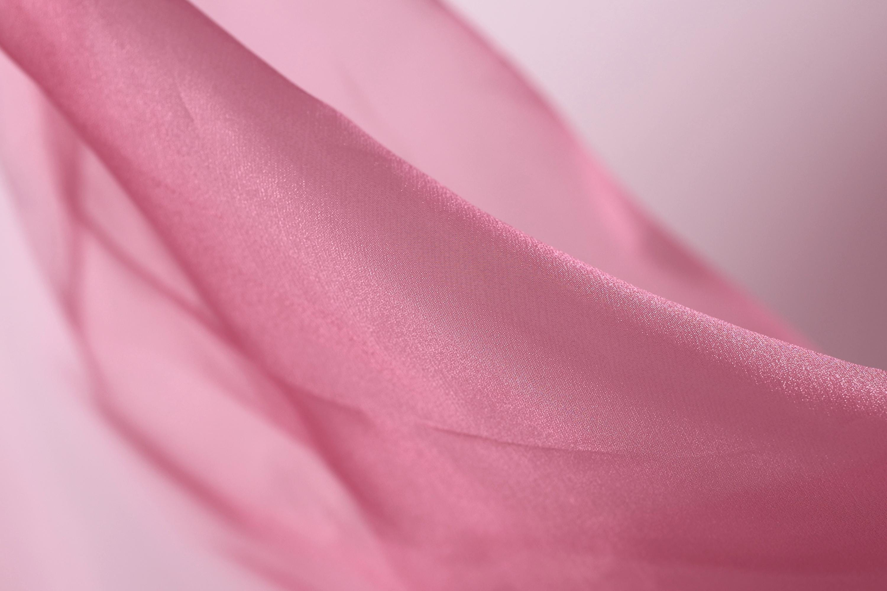 A close-up view of a soft, flowing pink fabric, possibly silk or chiffon, with a smooth and shiny texture.