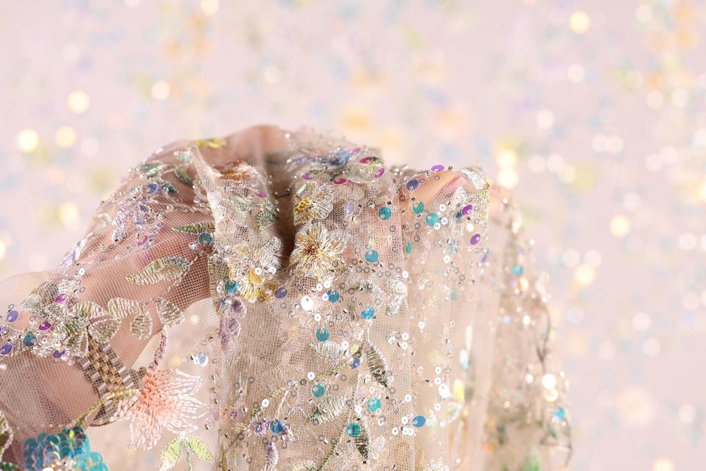 A hand holding a delicate, intricately embroidered fabric with a floral pattern and sequins.