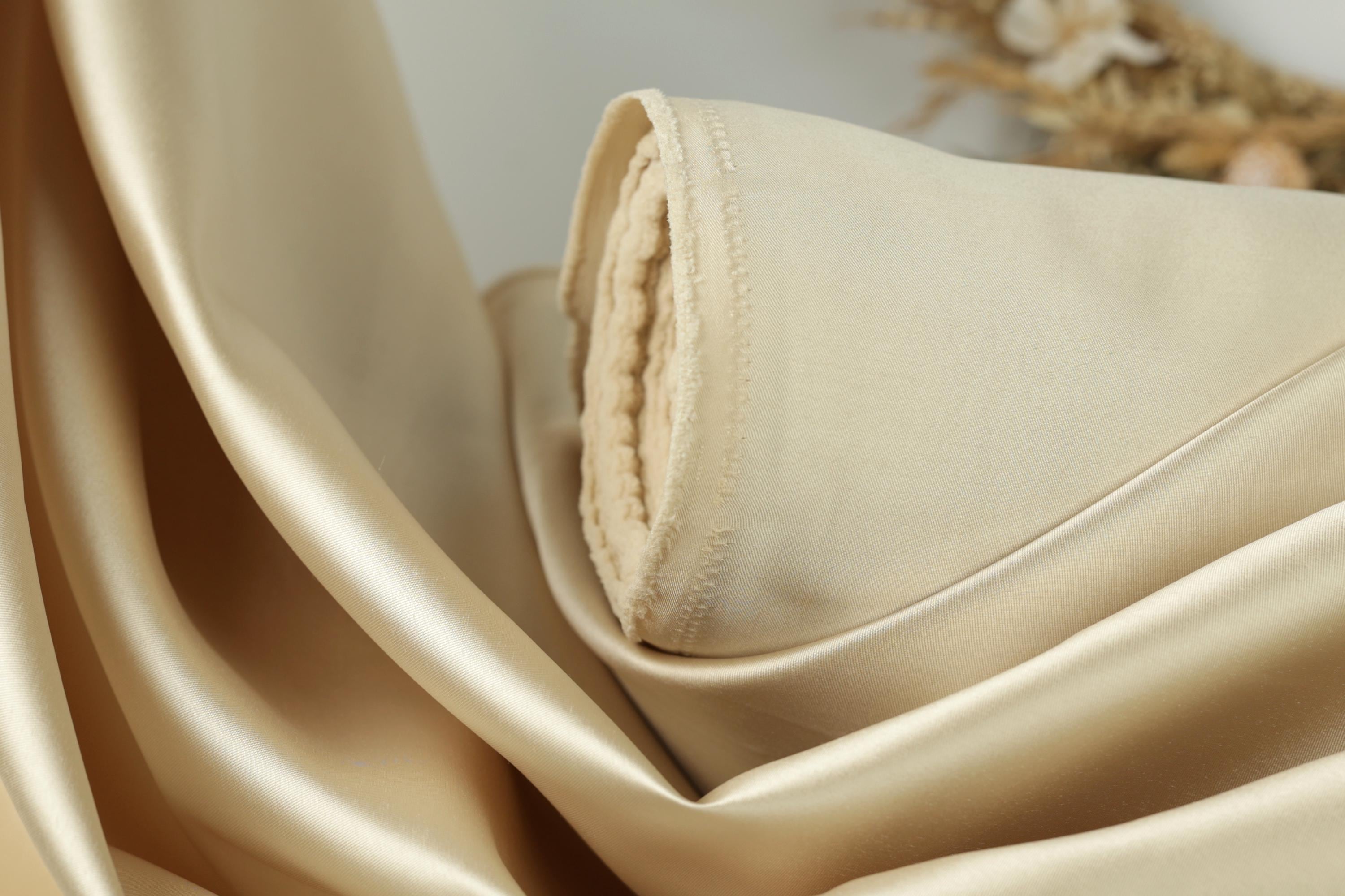 A close-up view of a piece of light-colored fabric, possibly silk or satin, with a folded edge and a small amount of fabric visible.